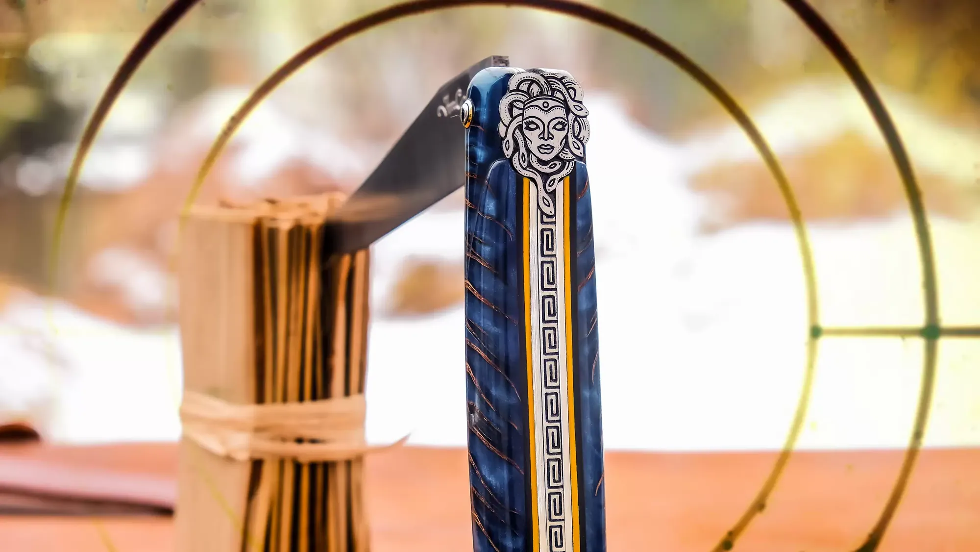 Laguiole-Taschenmesser mit blau gestreiftem Griff, aufgestellt in einem goldenen Ring