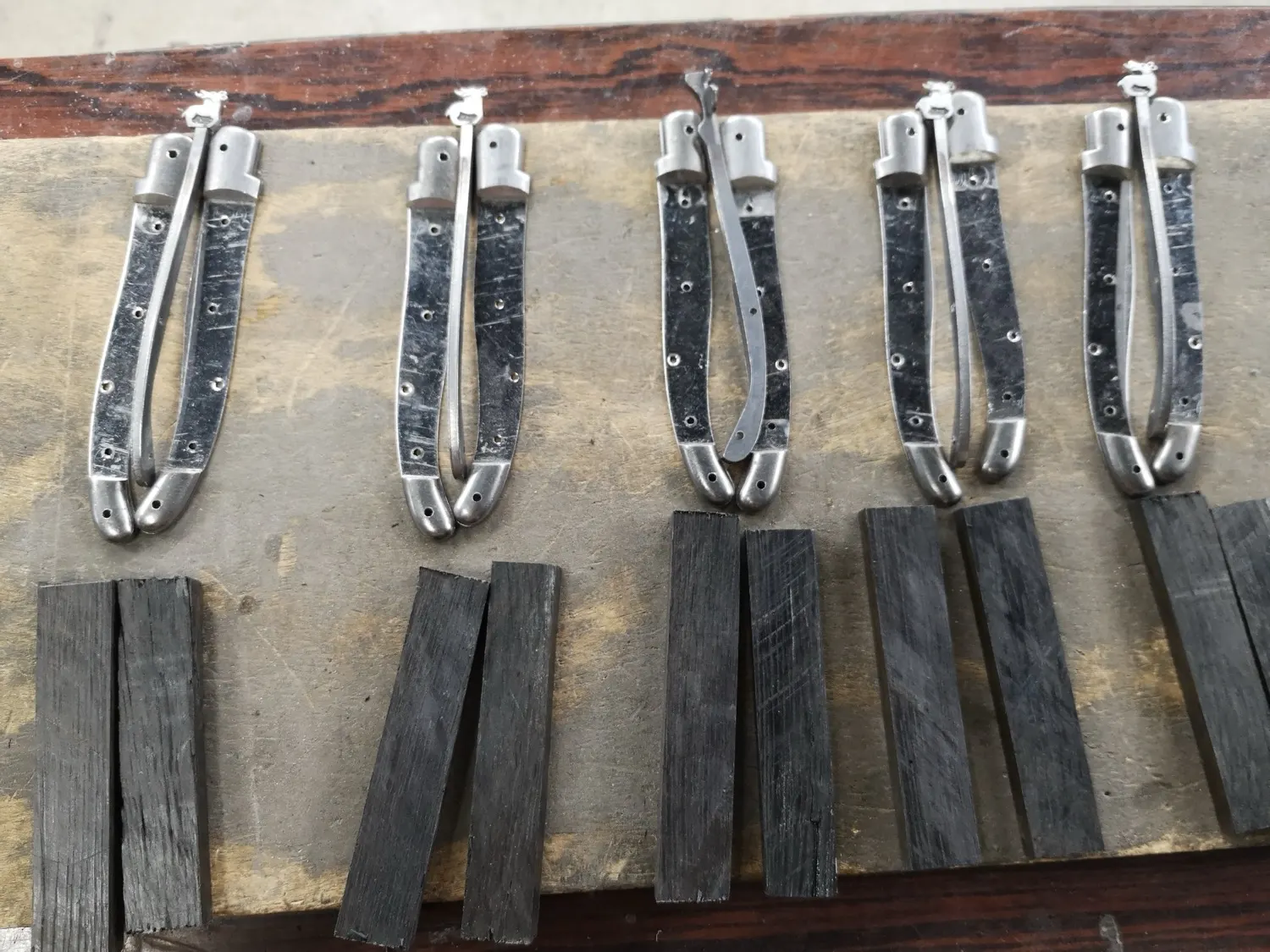 Fünf Messer im Rohbau, daneben die Griffschalen, die dazugehören. Jedes Paar bleibt bei seinem Messer, weil kein Holzstück zum anderen passt.
